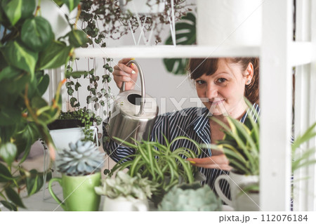 A young woman enjoys caring for flowers. Watering indoor plants and admiring them. 112076184