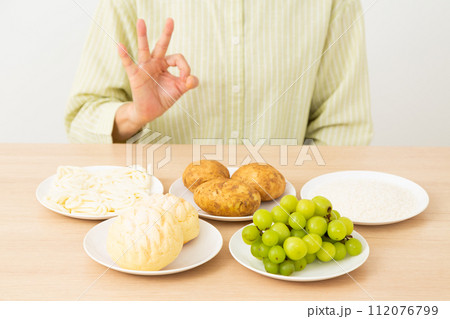 糖質を多く含む食品(炭水化物)と丸サインをするミドル女性 糖質を多く含む食品(炭水化物)と丸サインをするミドル女性 112076799
