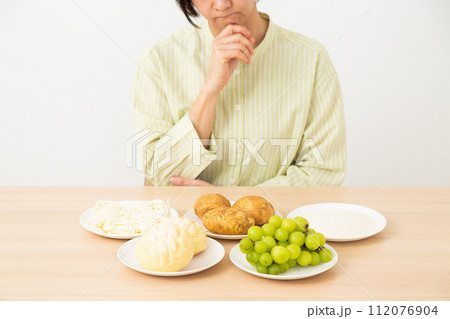 糖質を多く含む食品(炭水化物)と悩むミドル女性 糖質を多く含む食品(炭水化物)と悩むミドル女性 112076904