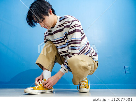 青い背景で黄色い靴を履く若い男性 112077601