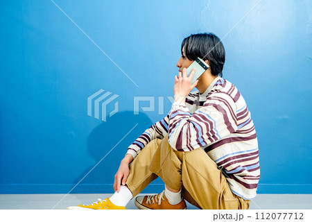 青い背景で電話をかけている若い男性 112077712