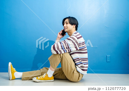 青い背景で電話をかけている若い男性 青い背景で電話をかけている若い男性 112077720