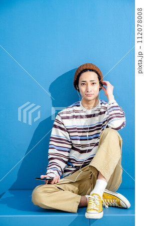 ブルーバックでメガネをかけて帽子をかぶりながらスマートフォンをいじっている若い男性 ブルーバックでメガネをかけて帽子をかぶりながらスマートフォンをいじっている若い男性 112078008