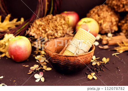 beeswax candle, bowl, apple and dry hydrangea flowers on brown background. Honey autumn cozy aroma candle for interior and tradition. Mockup, autumn composition, still life beeswax candle, bowl, apple and dry hydrangea flowers on brown background. Honey autumn cozy aroma candle for interior and tradition. Mockup, autumn composition, still life 112078782