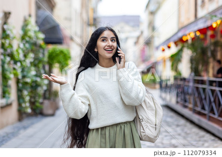 An Indian young smiling woman walks around the city, talks expressively on a mobile phone, has an emotional discussion, gestures with her hands. An Indian young smiling woman walks around the city, talks expressively on a mobile phone, has an emotional discussion, gestures with her hands. 112079334