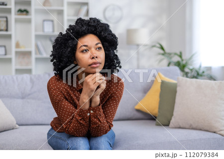 Sad and pensive African American woman sitting sullen at home and suffering from depression, crying after receiving bad news. 112079384