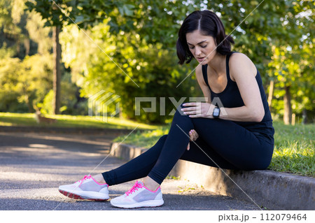 A dedicated woman runner pauses to check her activity on a smartwatch, capturing her fitness journey outdoors. 112079464