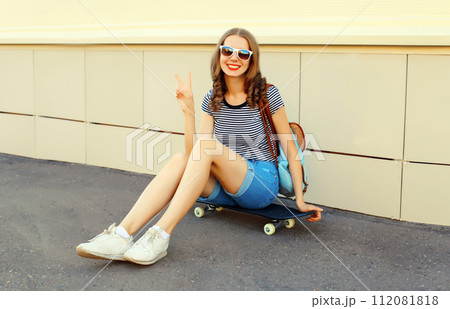 Portrait of cheerful young woman with skateboard in the city 112081818