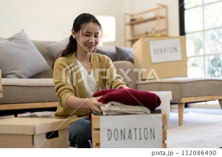 Woman asian holding donation box full with clothes and select clothes. Concept of donation and clothes recycling. Helping poor people 112086490