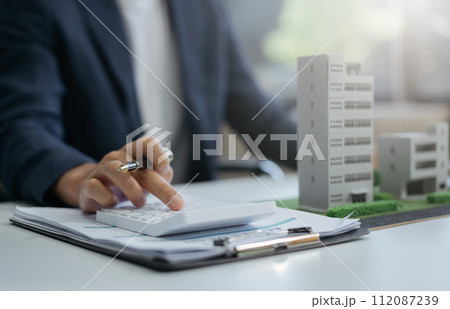 Home loan officer uses a calculator with a house plan on a wooden table. 112087239