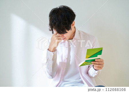 通帳を見て、がっかりする若い男性 通帳を見て、がっかりする若い男性 112088108
