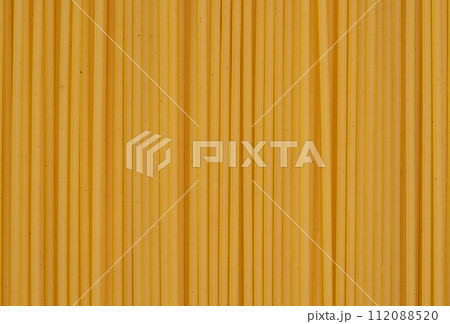 Parallel lines of uncooked spaghetti create a linear pattern on a yellow background, perfect for culinary and food themes. 112088520
