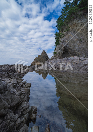 日本　青森県西津軽郡深浦町の仙北岩トンネル近くの水鏡に映った海岸の風景 112089013