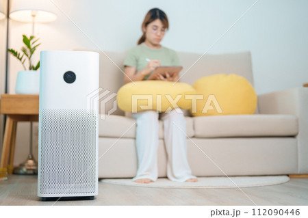 Air Purifier with woman relax and use tablet on sofa. Purification system for filter and cleaning dust PM2.5 HEPA and virus in home. Allergy, Pure air, health, Wellness lifestyle and Air Pollution Air Purifier with woman relax and use tablet on sofa. Purification system for filter and cleaning dust PM2.5 HEPA and virus in home. Allergy, Pure air, health, Wellness lifestyle and Air Pollution 112090446