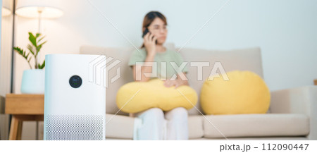 Air Purifier with woman relax and use smartphone on sofa. Purification system for filter and cleaning dust PM2.5 HEPA and virus in home. Allergy, Pure air, health, Wellness lifestyle and Air Pollution Air Purifier with woman relax and use smartphone on sofa. Purification system for filter and cleaning dust PM2.5 HEPA and virus in home. Allergy, Pure air, health, Wellness lifestyle and Air Pollution 112090447