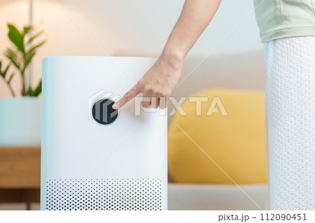 Woman turn on Air Purifier in living room. Purification system for filter and cleaning dust PM2.5 HEPA and virus in home. Allergy, Pure air, health lifestyle, Wellness life and Air Pollution 112090451