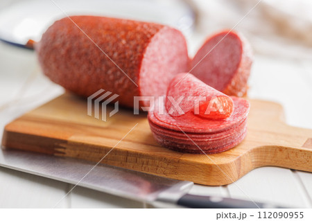 Sliced smoked salami sausages on cutting board on white table. 112090955