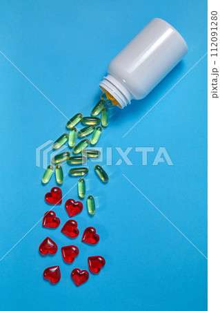 Yellow omega 3 gelatin tablets and red hearts spill out of a white jar on a blue background Yellow omega 3 gelatin tablets and red hearts spill out of a white jar on a blue background 112091280