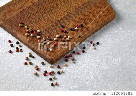 Wooden beige cutting board with scattered multicolored peppercorn peas on a gray stone countertop 112091283