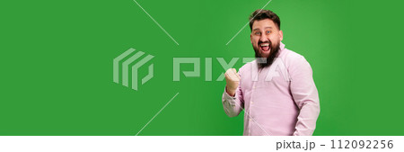 Banner. Young smiling man rejoice success and clenched fist against vibrant green studio background. Negative space to insert text. 112092256
