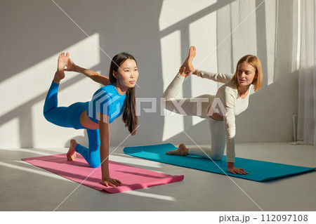 Yoga coach woman is teaching asian woman yoga and stretching. Concept of physical and mental health care, asian and caucasian ethnicity 112097108