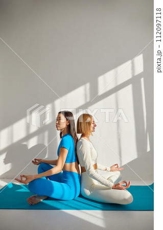 Two young women doing yoga meditation. Concept of physical and mental health care, asian and caucasian ethnicity 112097118