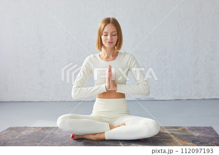 Woman practicing yoga and meditation in lotus pose on yoga mat, relaxed with closed eyes. Mindful meditation concept. Woman practicing yoga and meditation in lotus pose on yoga mat, relaxed with closed eyes. Mindful meditation concept. 112097193