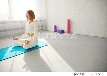 Woman practicing yoga and meditation in lotus pose on yoga mat, relaxed with closed eyes. Mindful meditation concept. 112097202