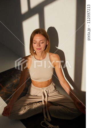 Woman practicing yoga and meditation in lotus pose on yoga mat, relaxed. Mindful meditation concept. Wellbeing 112097213