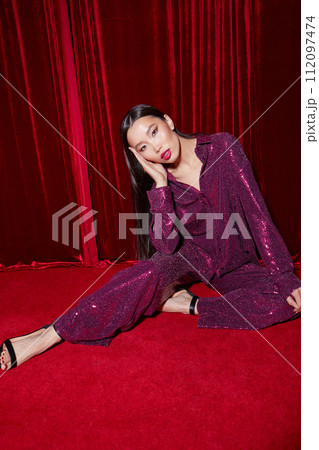 Fashion asian female model in burgundy glitter suit, on red fabric background. 112097474