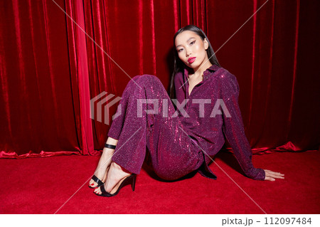 Fashion asian female model in burgundy glitter suit, on red fabric background. Fashion asian female model in burgundy glitter suit, on red fabric background. 112097484