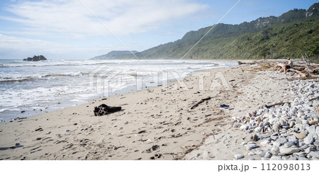 Man siting on the edge of rough deserted beach with rainforest in background, New Zealand Man siting on the edge of rough deserted beach with rainforest in background, New Zealand 112098013