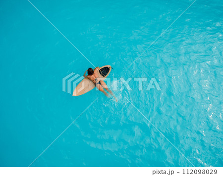 Sexy surf girl in bikini with surfboard in blue ocean. Aerial view Sexy surf girl in bikini with surfboard in blue ocean. Aerial view 112098029