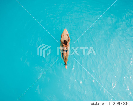 Sexy girl in bikini relaxing on surfboard in sea. Aerial view of woman during surfing 112098030