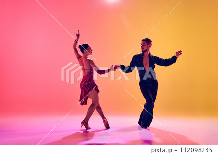 Male and female dancers performing a Latin dance in stylish clothes against gradient pink yellow background in neon light Male and female dancers performing a Latin dance in stylish clothes against gradient pink yellow background in neon light 112098235