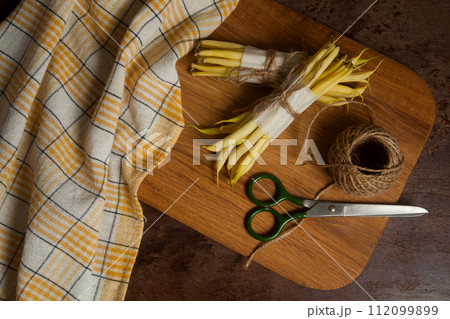 Cutting board with two bunch and several pods of flat runner bean pods heap with yellow kitchen towel, scissors and ball of thread on wooden background. . Cutting board with two bunch and several pods of flat runner bean pods heap with yellow kitchen towel, scissors and ball of thread on wooden background. . 112099899