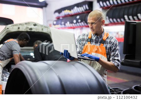 Mechanic man with laptop making car diagnostics at service 112100432
