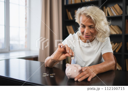 Saving money investment for future. Senior adult mature woman putting money coin in piggy bank. Old grandmother counting saving money planning retirement budget. Investment banking concept Saving money investment for future. Senior adult mature woman putting money coin in piggy bank. Old grandmother counting saving money planning retirement budget. Investment banking concept 112100715