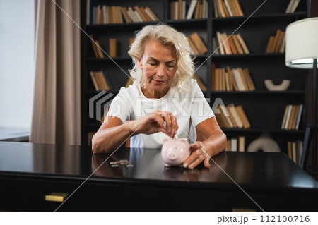 Saving money investment for future. Senior adult mature woman putting money coin in piggy bank. Old grandmother counting saving money planning retirement budget. Investment banking concept 112100716
