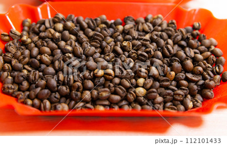 Roasted selective arabica coffee beans are in red plastic tray, close-up 112101433