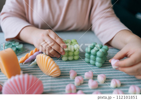 Cropped shot of unrecognizable female artisan sitting at desk with finished various candles after create. Process of making handmade natural scented candle. Creative occupation of making DIY candles. Cropped shot of unrecognizable female artisan sitting at desk with finished various candles after create. Process of making handmade natural scented candle. Creative occupation of making DIY candles. 112101851