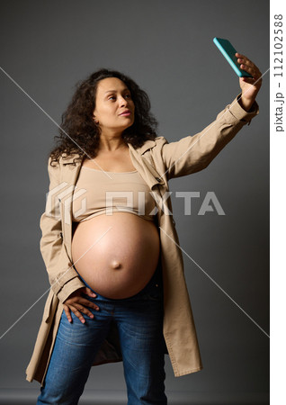 Stylish pregnant woman taking selfie on smartphone, sharing her lifestyle in last trimester of pregnancy on social media 112102588