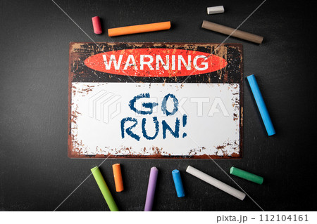Go Run. Metal warning sign and colored pieces of chalk on a dark chalkboard background Go Run. Metal warning sign and colored pieces of chalk on a dark chalkboard background 112104161
