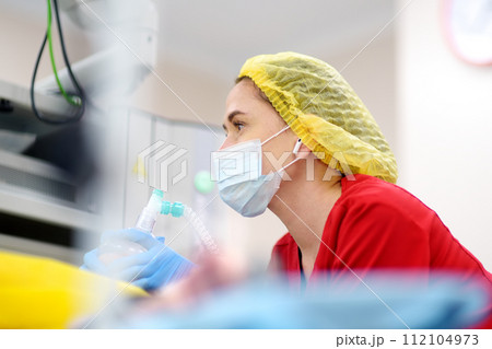 Female anesthesiologist injects anesthesia into patient face mask. General sedation while surgery operation. Paramedic putting oxygen mask for breathing and ventilation of person during resuscitation Female anesthesiologist injects anesthesia into patient face mask. General sedation while surgery operation. Paramedic putting oxygen mask for breathing and ventilation of person during resuscitation 112104973