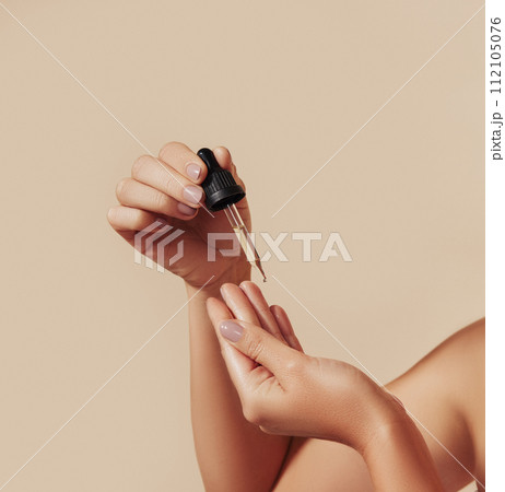Cropped shot of woman hands holding a pipette against pastel backdrop. Female hands holding a pipette with liquid serum testing consistency with fingers. 112105076