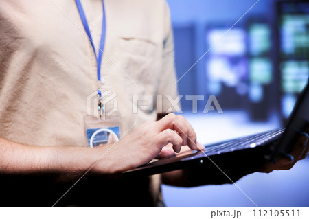 Worker in front of blurry background supercomputers delivering web content to online customers. Repairman in server room using laptop to make sure critical systems are working errorless, close up Worker in front of blurry background supercomputers delivering web content to online customers. Repairman in server room using laptop to make sure critical systems are working errorless, close up 112105511
