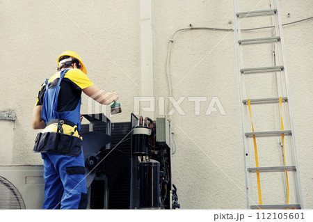 Certified technician commissioned by home owner for annual air conditioner routine cleaning and maintenance, using soft dusting brush to remove built up layer of dirt and dust from internal parts Certified technician commissioned by home owner for annual air conditioner routine cleaning and maintenance, using soft dusting brush to remove built up layer of dirt and dust from internal parts 112105601