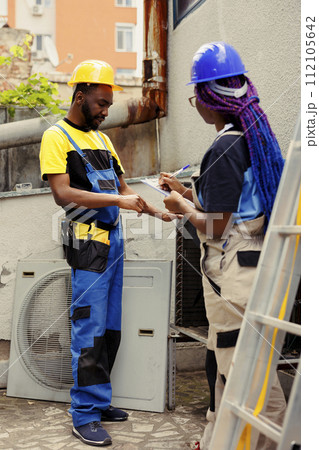 Efficient technicians repairing and maintaining condenser heating and ventilation. Knowleadgeable engineers hired for outdoor air conditioner routine checkup, writing report on clipboard Efficient technicians repairing and maintaining condenser heating and ventilation. Knowleadgeable engineers hired for outdoor air conditioner routine checkup, writing report on clipboard 112105642