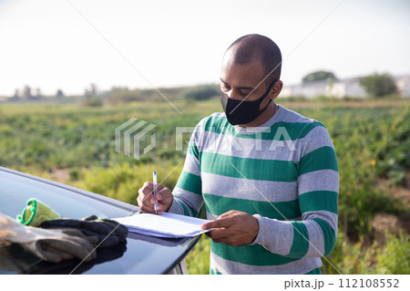 Farmer in protective mask signing papers near car 112108552