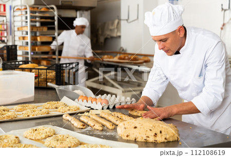 Male baker working with dough forming baguettes Male baker working with dough forming baguettes 112108619